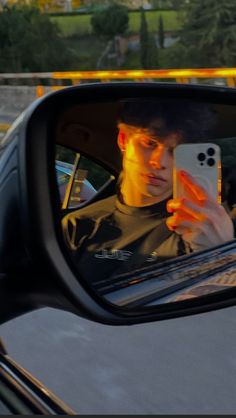 a man taking a selfie in the side mirror of a car with his cell phone