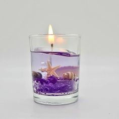 a candle that is inside of a glass filled with water and purple sand in it