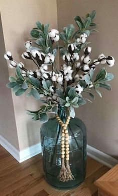 a vase filled with cotton and greenery on top of a wooden floor