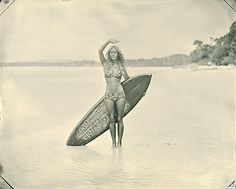 a woman holding a surfboard standing in the water on top of a sandy beach