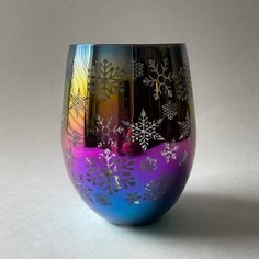 a multicolored glass with snowflakes on the outside and inside, sitting on a white surface