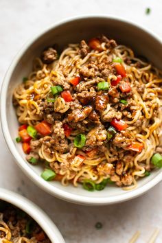 two bowls filled with noodles and meat on top of a white countertop next to chopsticks