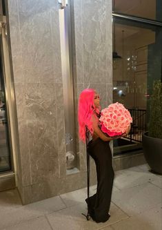 a woman with pink hair is holding a large flower in front of a building entrance