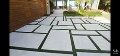 an outdoor walkway with grass on the sides and white tiles on the ground in front of a house