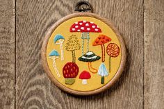 a small embroidery project with mushrooms and umbrellas on yellow fabric hanging from a wooden hoop