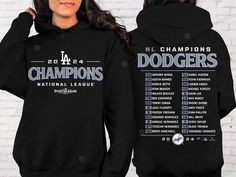 the los angeles dodgers women's black 2013 national league champs hoodie is shown in front of a white brick wall