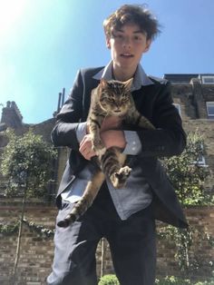 a young man holding a cat in his arms while wearing a suit and smiling at the camera