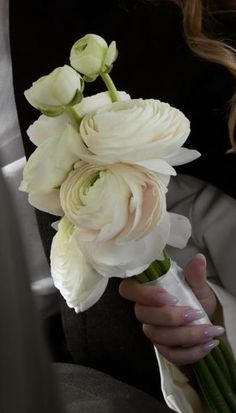 a bouquet of white flowers being held by a woman in a black jacket and dress