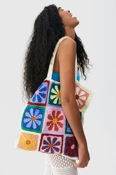 a woman holding a multicolored crocheted bag with flowers on the front