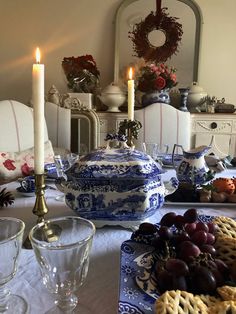 a dining room table is set with blue and white dishes, crackers, grapes, cookies, and candles