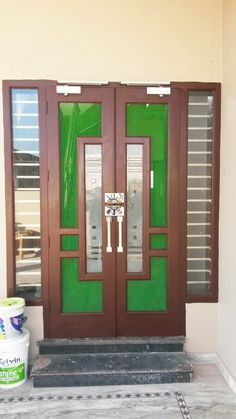 the front door is painted green and has two glass panels on each side, along with a bucket of paint next to it