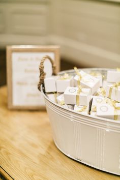 small white boxes with gold bows are in a metal container on a table next to a card