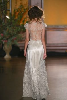 a woman walking down a runway wearing a white dress with sheer back and lace detailing