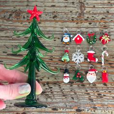 a hand holding a christmas tree shaped keychain next to other ornaments on a wooden table