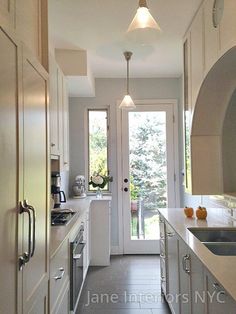 a long narrow kitchen with white cabinets and stainless steel appliances on the countertops, along with an oven