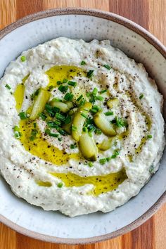 a white bowl filled with hummus and green onions on top of a wooden table