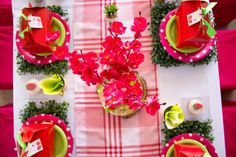 the table is set with red and green plates, napkins, and flower centerpieces