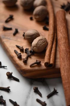 an assortment of spices on a cutting board next to cinnamon sticks and cloves