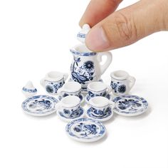 a hand is picking up a blue and white porcelain tea set