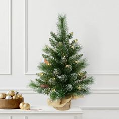 a small christmas tree sitting on top of a white table next to a wooden bowl