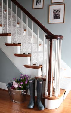 a bucket with flowers and rain boots sitting on the ground in front of a stair case