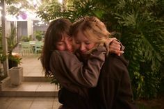 two women hugging each other in front of some plants