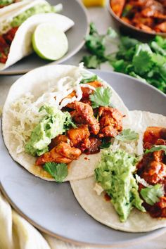 two tacos with meat, guacamole and cilantro on the side