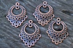 three pairs of copper toned metal earrings on a wooden table with wood grained surface