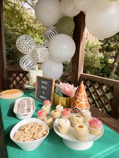 a table topped with lots of cupcakes and desserts next to white balloons