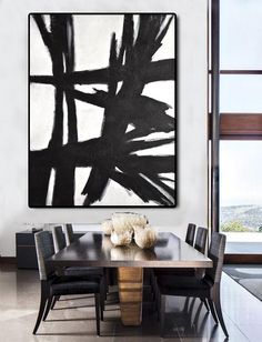 a black and white abstract painting hangs above a dining room table with chairs around it