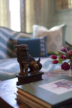 a wooden table topped with a vase filled with flowers and a small dog figurine