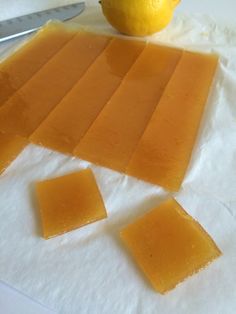 pieces of cheese sitting on top of white paper next to a knife and an orange