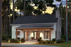 a small white house surrounded by trees and bushes at night with lights on the front door