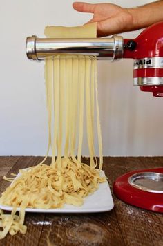 a person is pouring pasta into a white plate on a wooden table with a red mixer