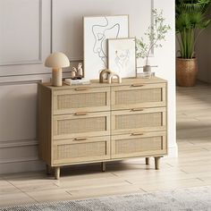 a wooden dresser sitting next to a white wall with pictures on it and plants in the corner