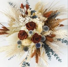 an arrangement of dried flowers and foliage on a white tablecloth with red roses in the center