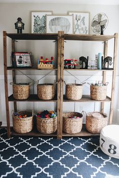 a shelf with baskets and toys on it in a living room next to a blue rug