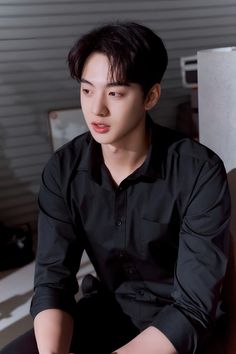 a young man sitting on top of a bed in a black shirt and dark pants