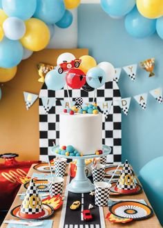 a birthday party with balloons, cake and race cars on the table in front of it