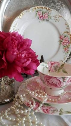 a pink flower sitting on top of a table next to a cup and saucer