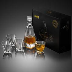 an assortment of whiskey glasses and decanter in front of a black box on a reflective surface