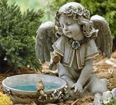 an angel figurine sitting on the ground next to a bird bath