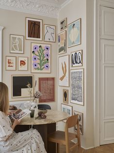 a woman sitting at a table in front of a wall covered with pictures and flowers