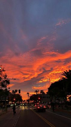 the sky is red and orange as cars drive down the street