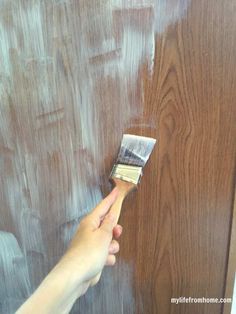 a person holding a paintbrush in their hand and painting the wall with brown wood