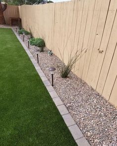 a backyard with grass, rocks and plants in the corner next to a fenced in area