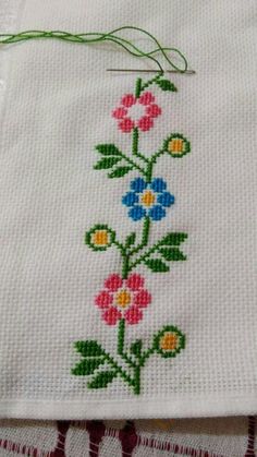 a cross stitched flower design on a white cloth with a green string hanging from it