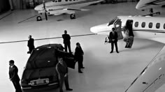 several people standing in front of an airplane with a car parked next to the plane