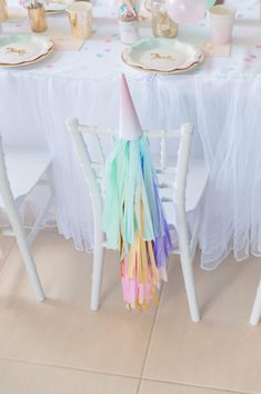 a table set up for a party with white chairs and colorful streamers on it