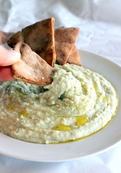 a person dipping crackers into a bowl of hummus